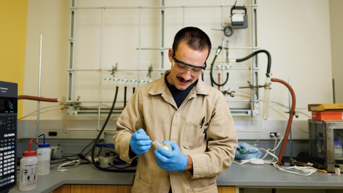 Student Sal Deguara wears protective lab gear as he examines a chemical compound.