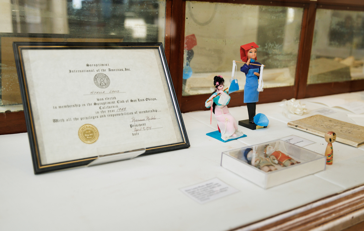 Antique Chinese dolls and a certificate addressed to Stella Louis sit in a display case.